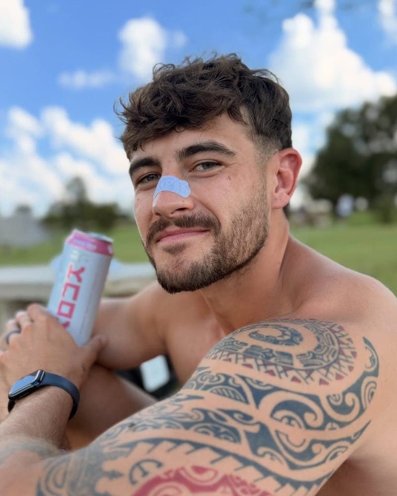 Man outdoors wearing a RestUp nasal strip, holding a drink